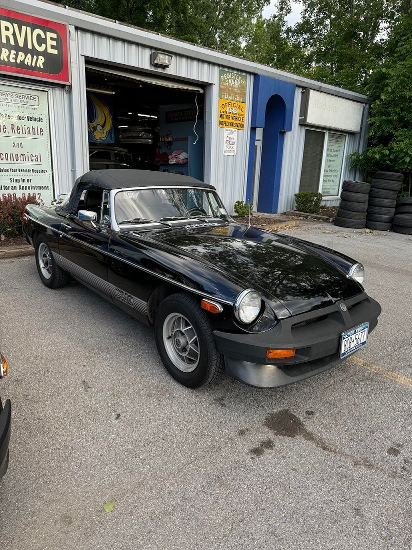 Black MG MGB convertible parked in front of a car repair shop.