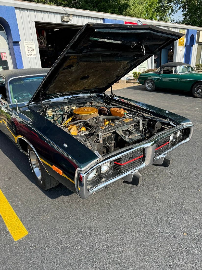 Dark green classic car with hood open in front of a repair shop.