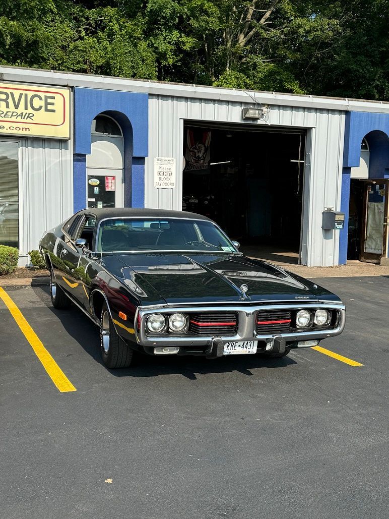 Black classic car parked in front of a blue and white auto service shop.