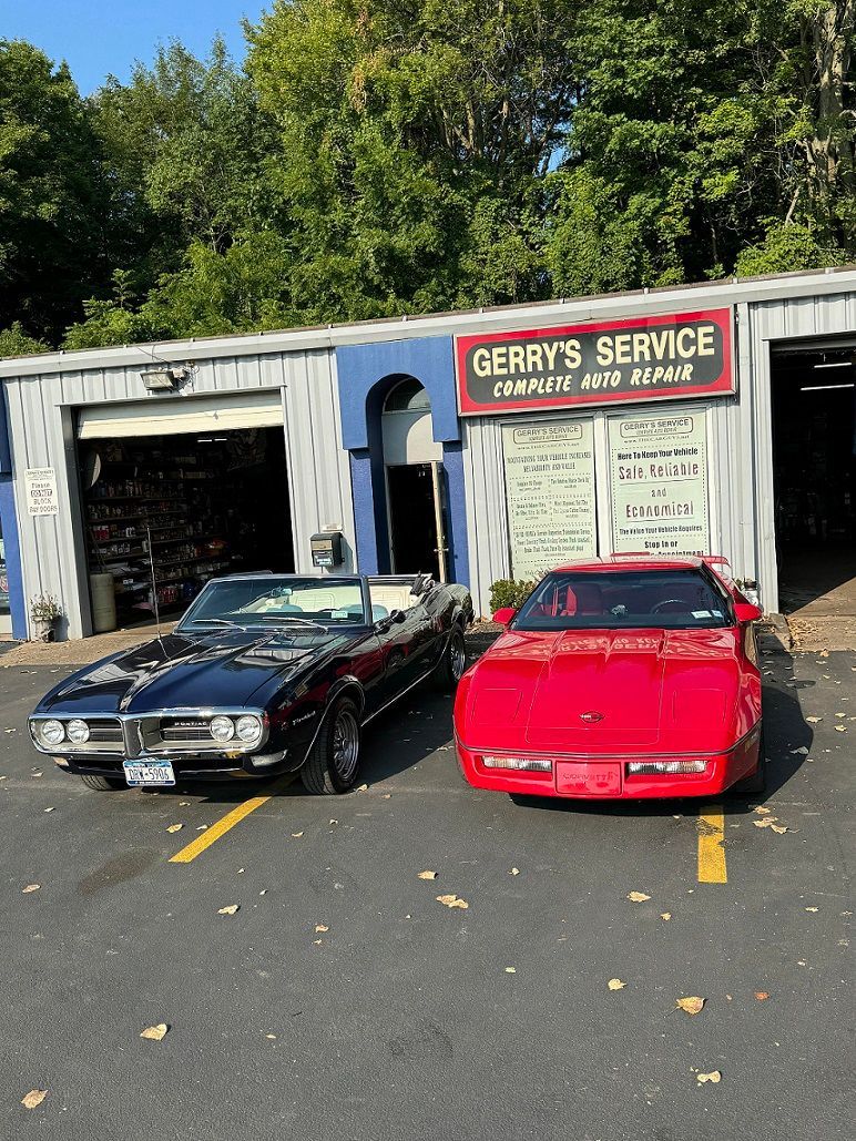 Two Pontiac Firebirds parked in front of an auto repair shop. Black convertible and red coupe.