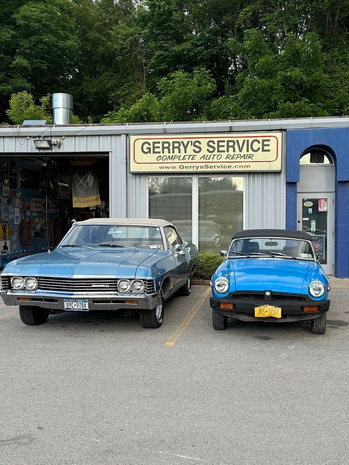 Two blue cars parked in front of Gerry's Service, an auto repair shop with a tan sign.