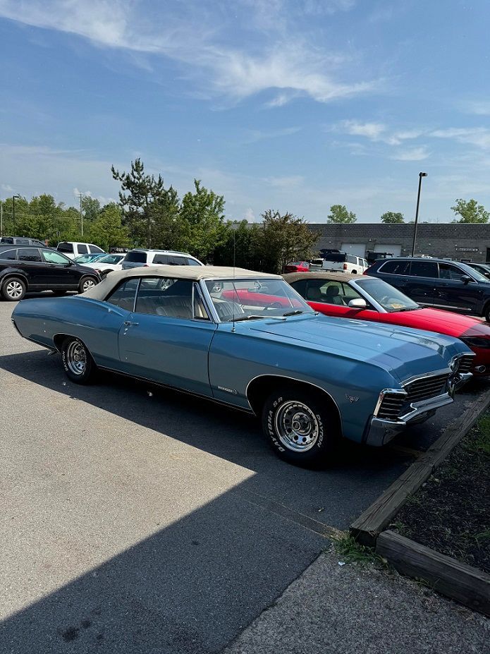 Blue convertible car parked on asphalt, sunny day. White roof, chrome details, and other vehicles in the background.