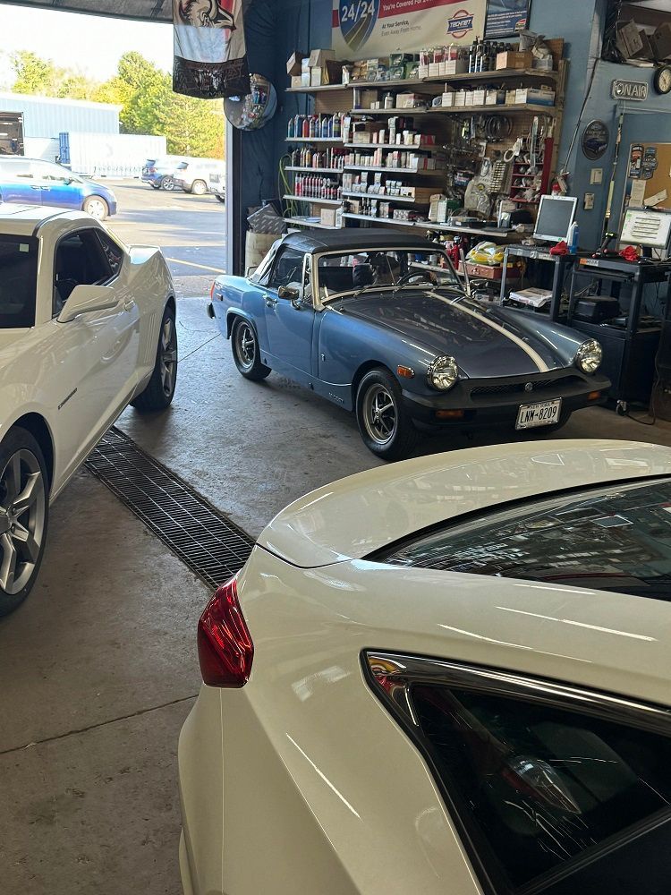 Cars in a garage; a white sports car, blue convertible, and a white sedan are parked inside.