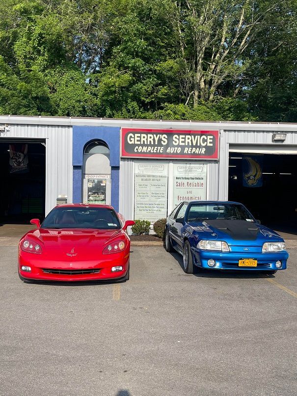 Red Corvette and blue Mustang parked outside Gerry's Service, a car repair shop.