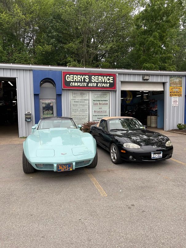 A light blue Corvette and a black convertible parked in front of Gerry's Service auto shop.