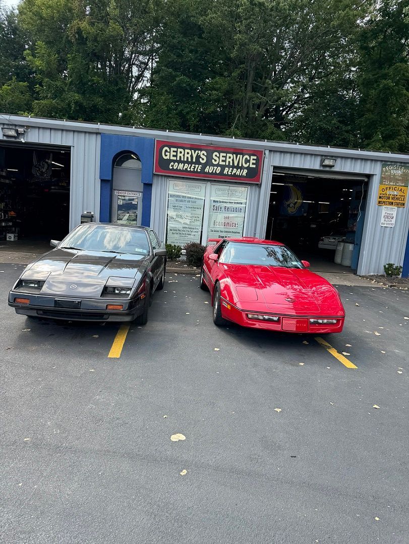 Two red and black sports cars parked in front of a blue auto repair shop called Gerry’s Service.