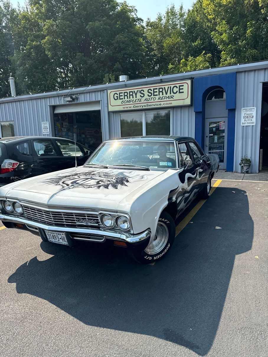 Silver and black classic car parked outside Gerry's Service garage on a sunny day.