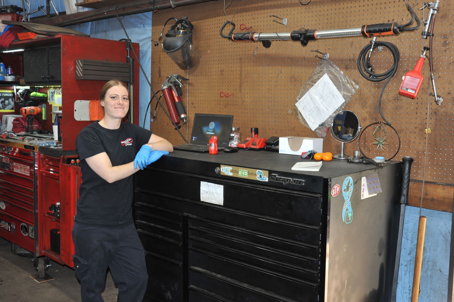 Woman in work clothes standing by a black tool chest in a workshop.