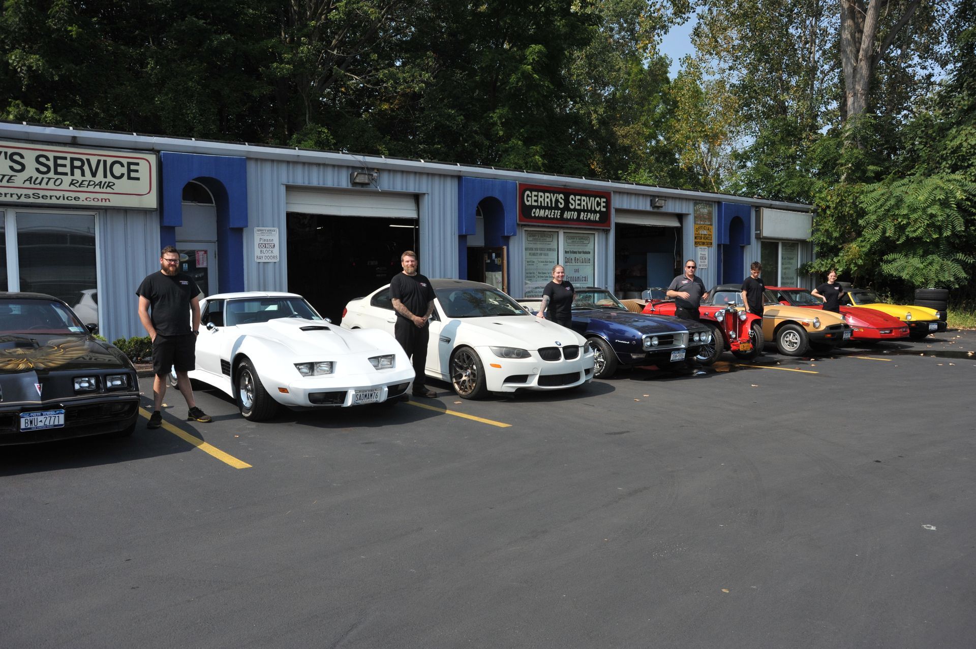 Cars parked in front of an auto shop. Several people stand near the vehicles.