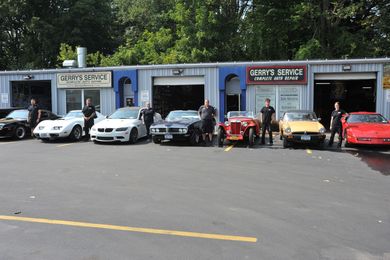 Cars and mechanics pose in front of a garage, a sunny day.