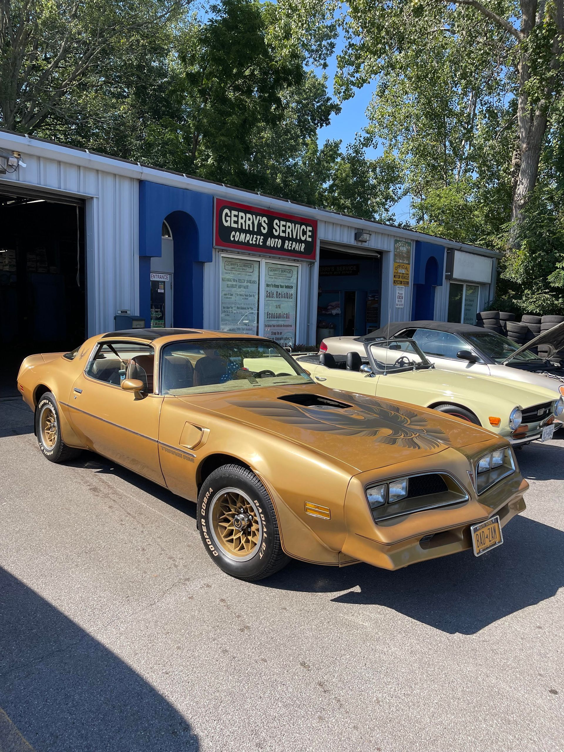 Gold Pontiac Firebird Trans Am parked in front of a blue and white auto shop.