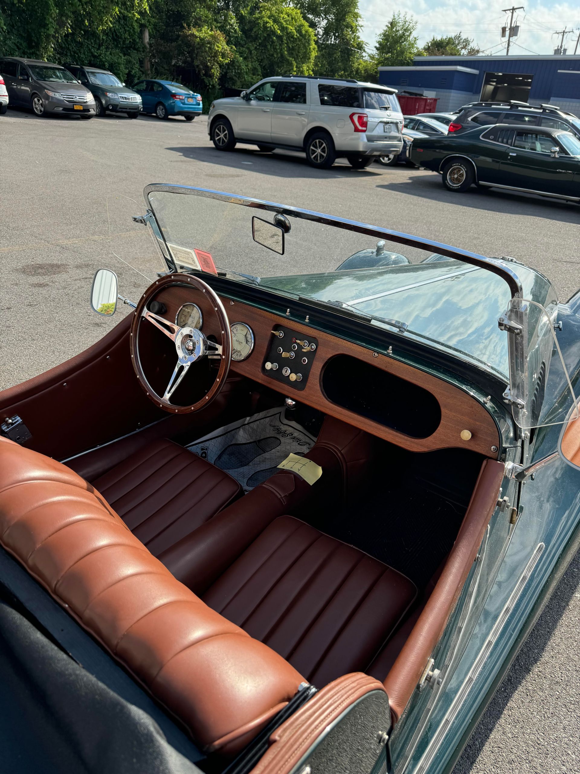 Interior of a classic green Morgan sports car with brown leather seats and wooden dashboard, parked outside.
