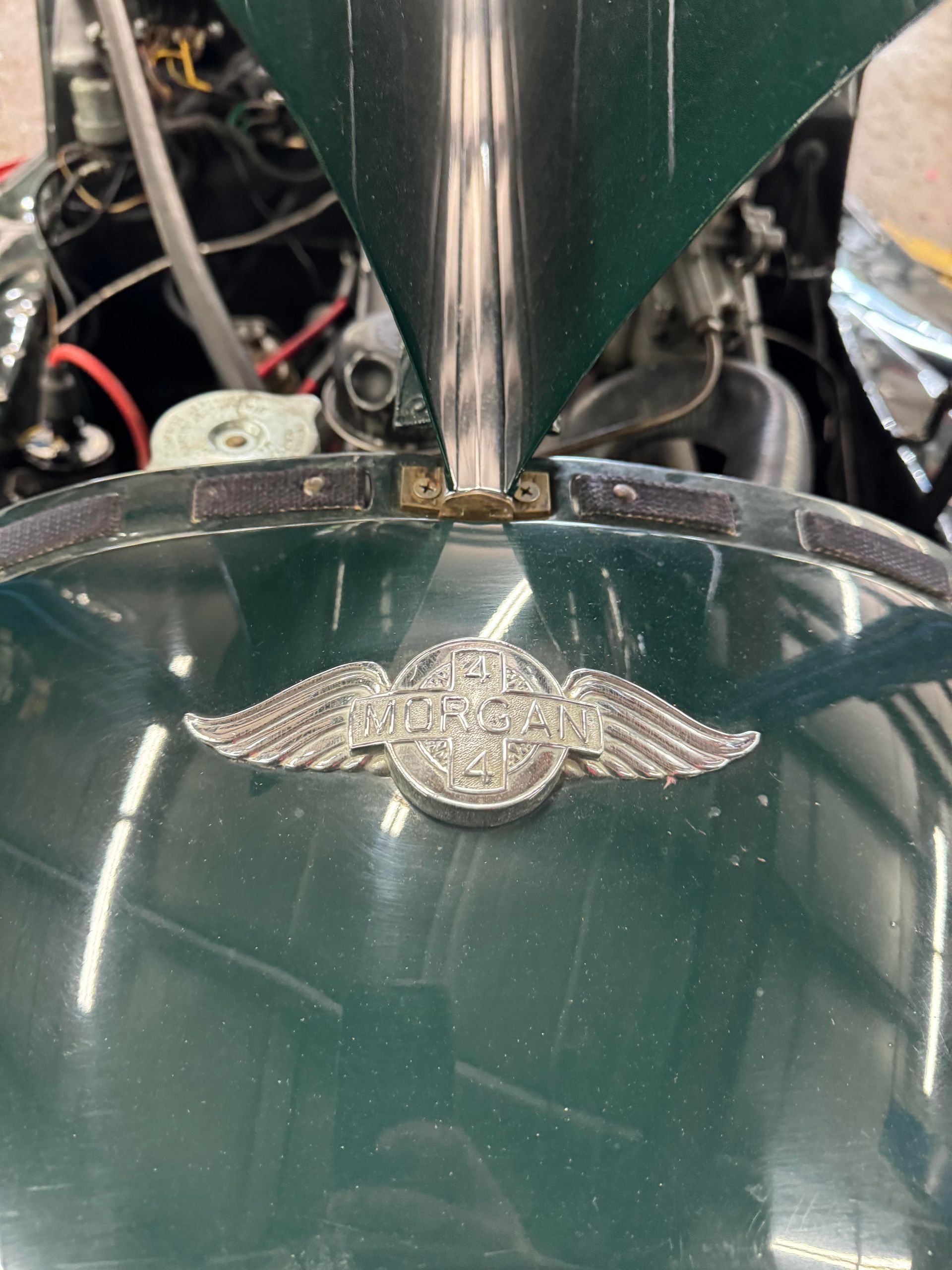 Green car hood with silver winged emblem, and chrome hood ornament.