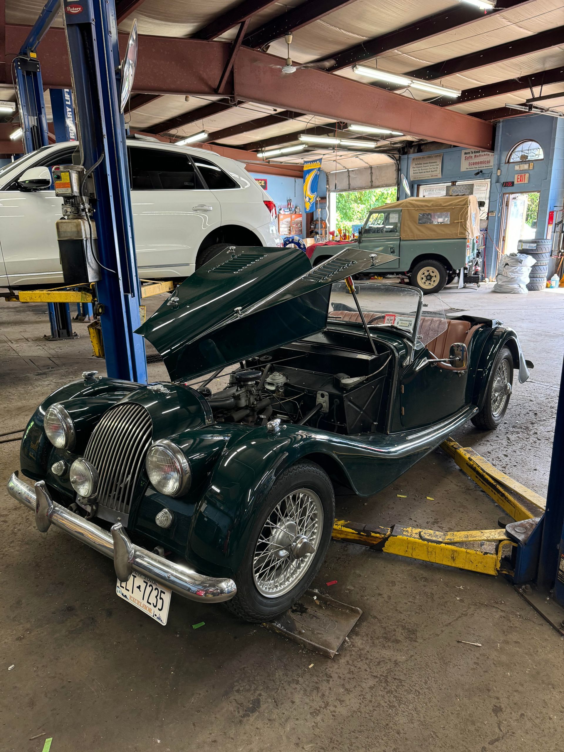 Green vintage Morgan sports car on a lift in a garage, hood open.
