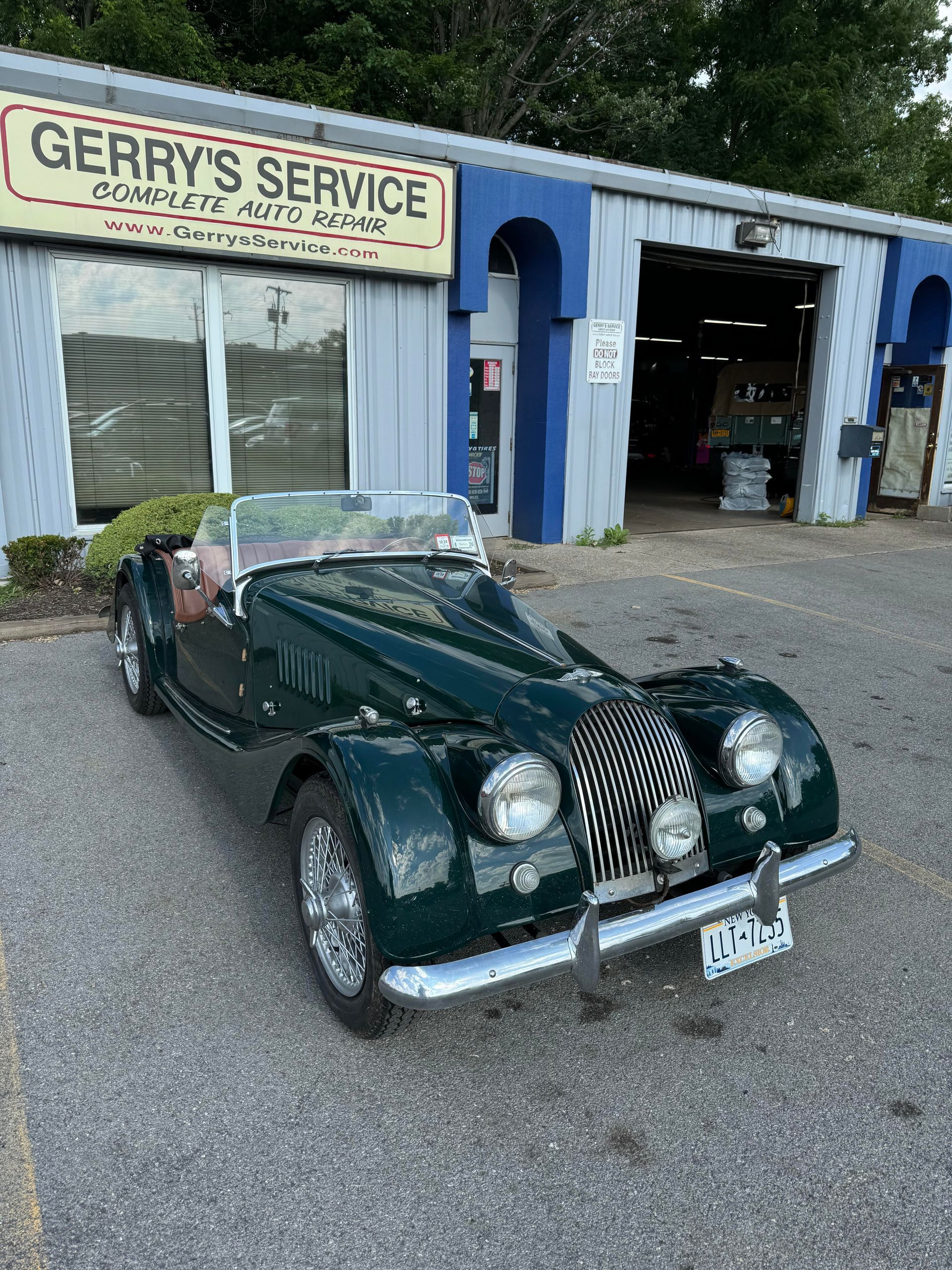 Green Morgan sports car parked outside Gerry's Service garage with open bay.