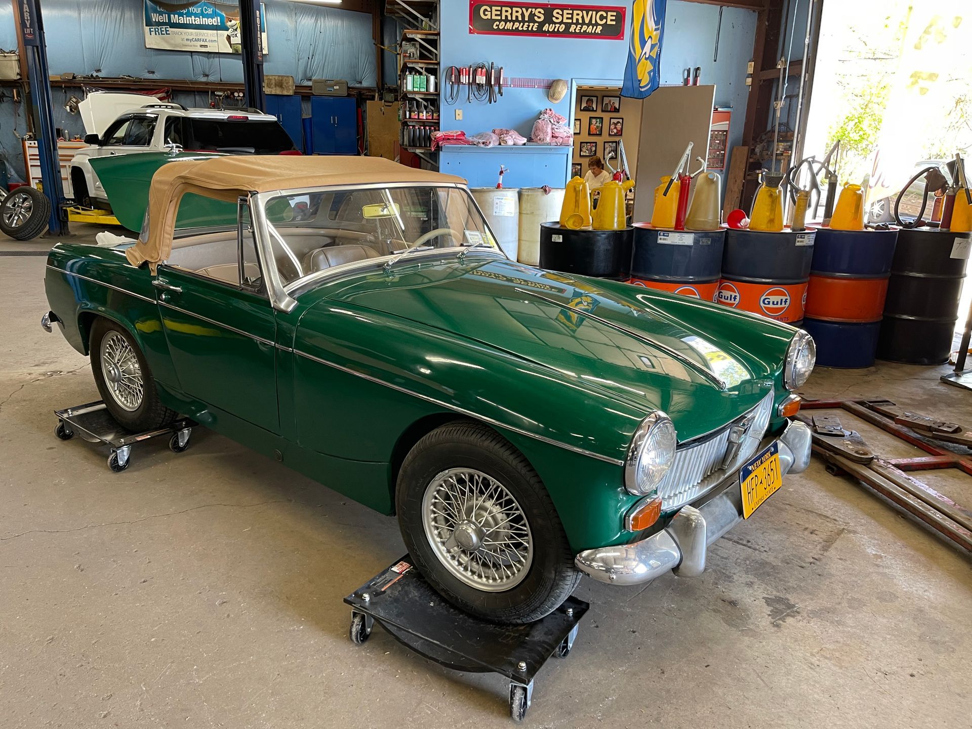 Green classic convertible car on dollies in a repair shop.