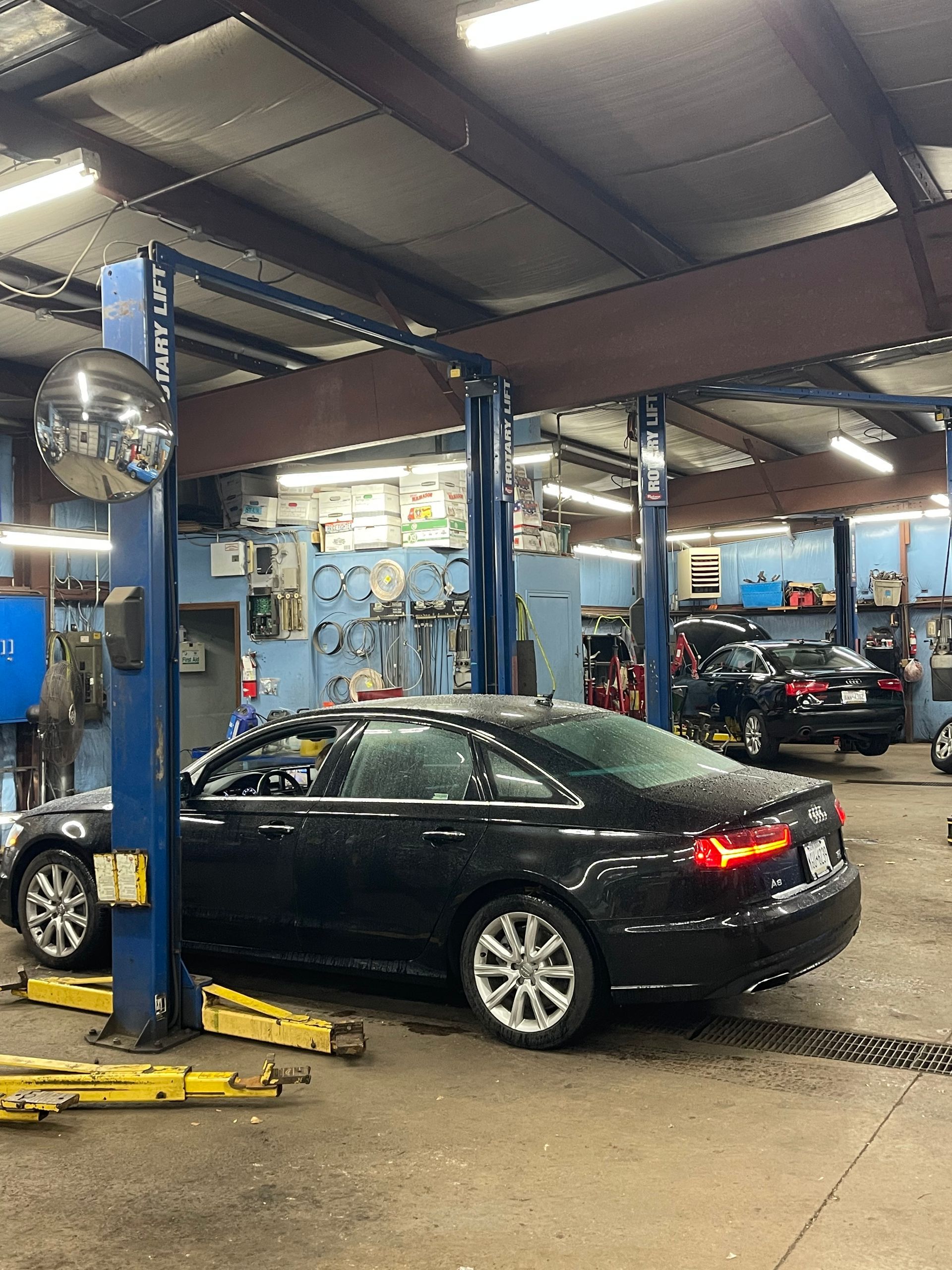Black car on a lift in a repair shop, other cars and equipment visible.