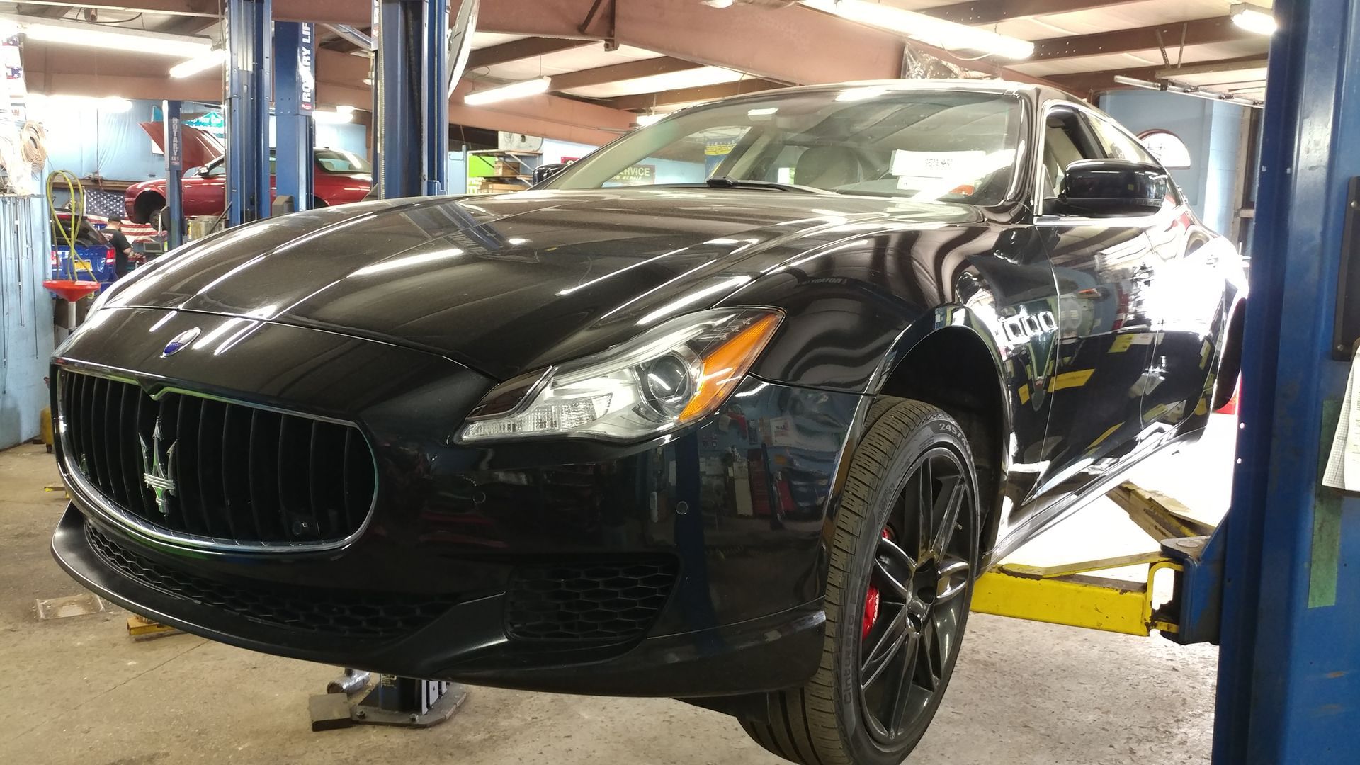 Black Maserati sedan raised on a car lift in a repair shop.