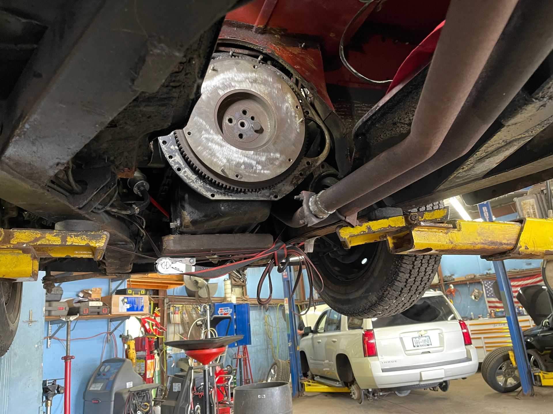 Undercarriage of a vehicle on a lift, exposing the engine's flywheel and exhaust components.