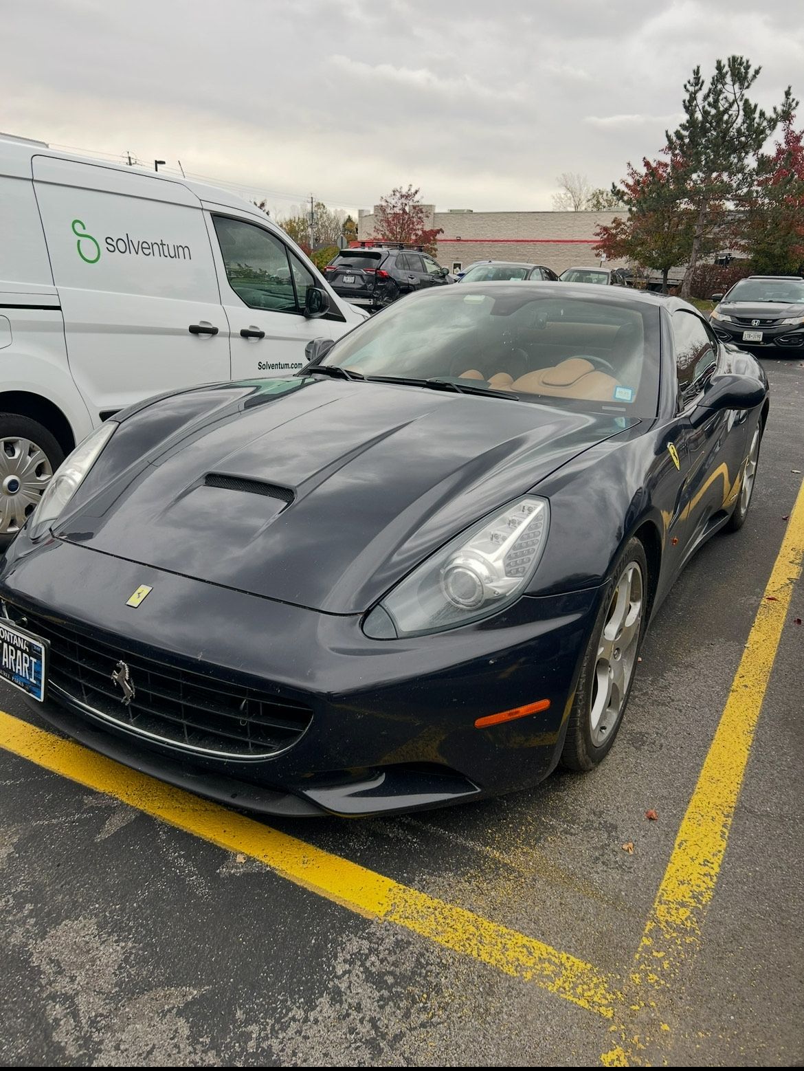 Dark blue Ferrari California parked in a parking lot. Cloudy sky.