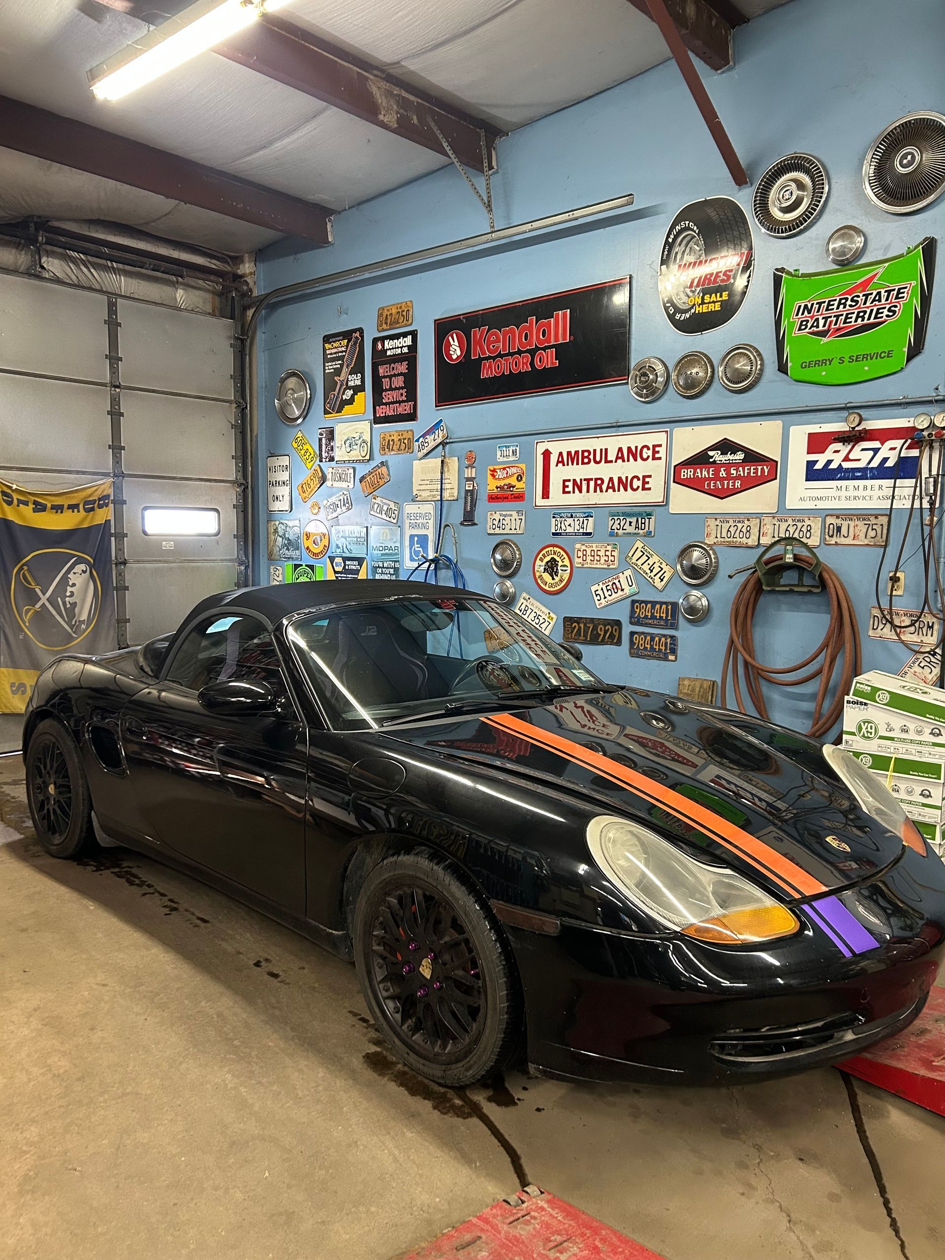Black Porsche sports car with colorful stripes parked in a garage with vintage signs on the wall.