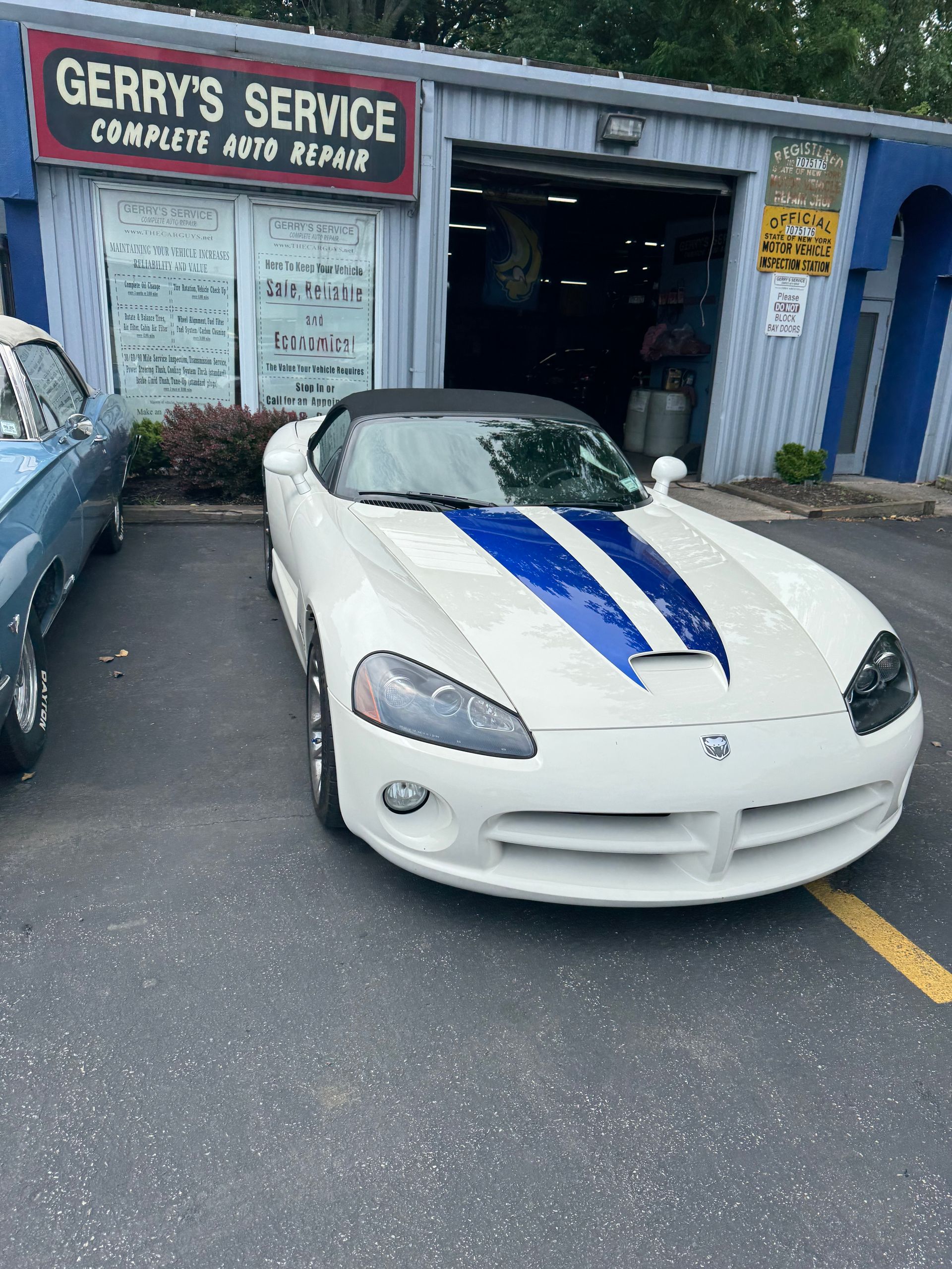 White Dodge Viper with blue racing stripes parked in front of an auto repair shop.