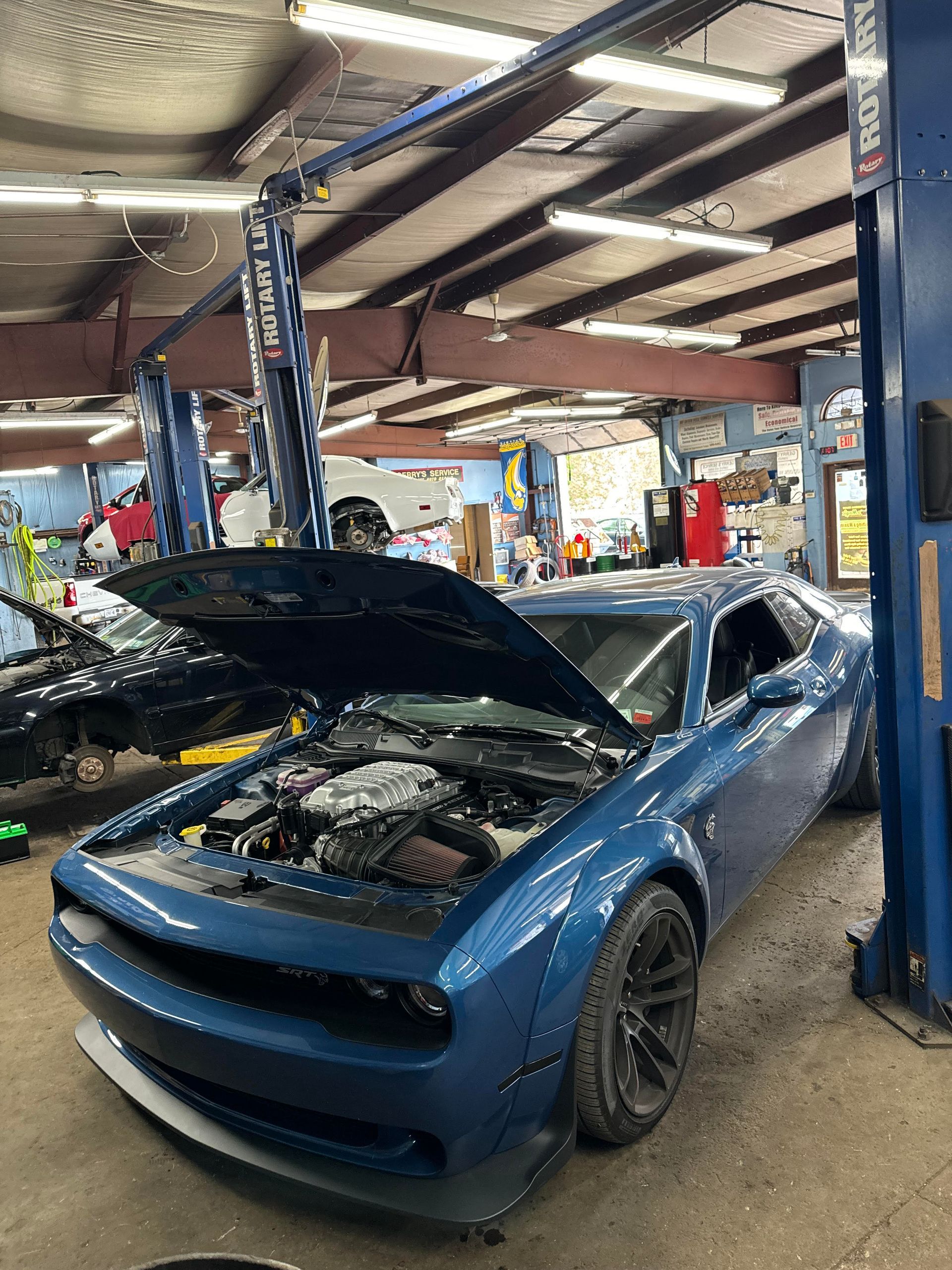 Blue Dodge Challenger with open hood in a garage, being worked on.