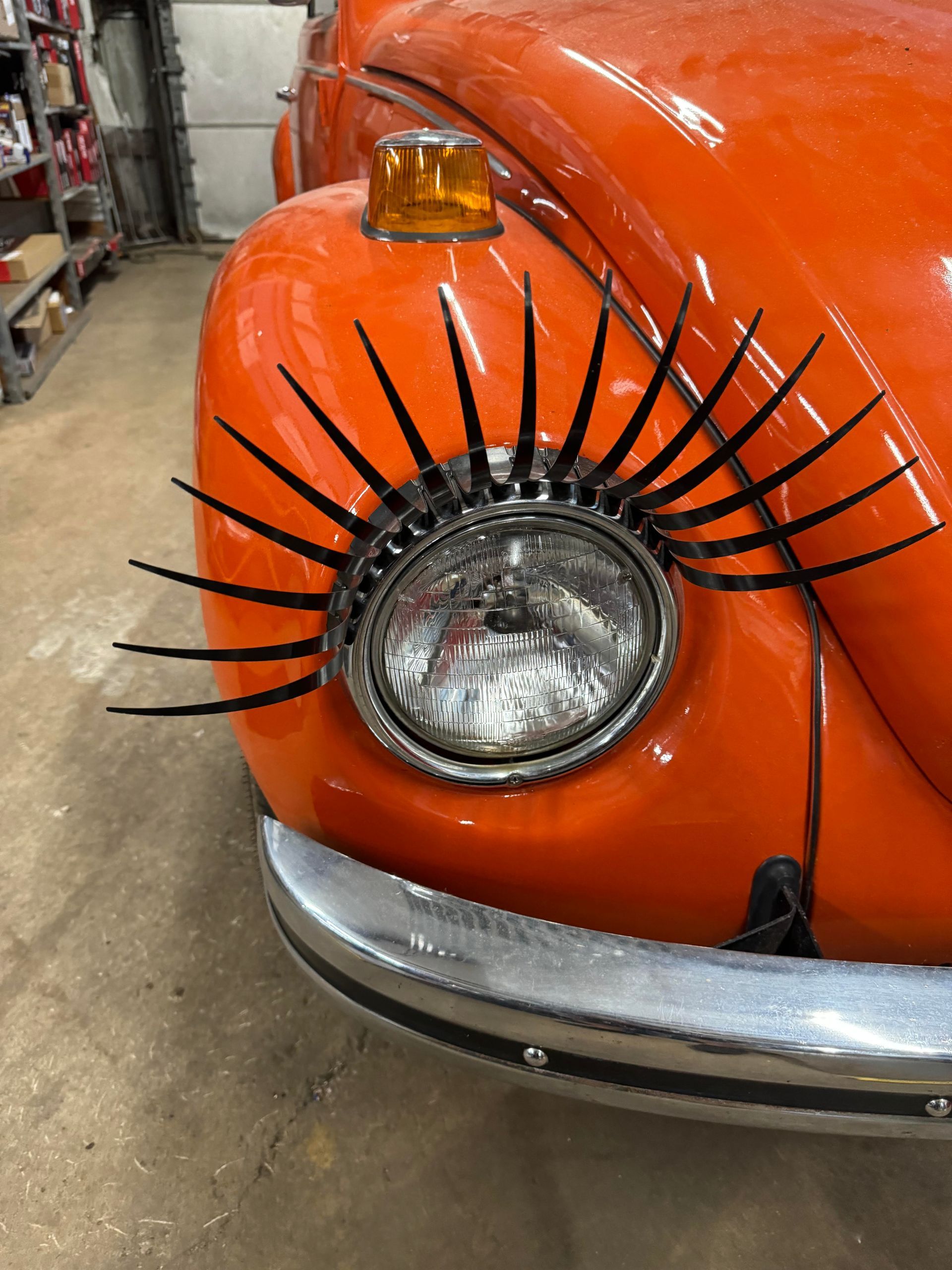 Orange Volkswagen Beetle with black eyelashes on headlight.