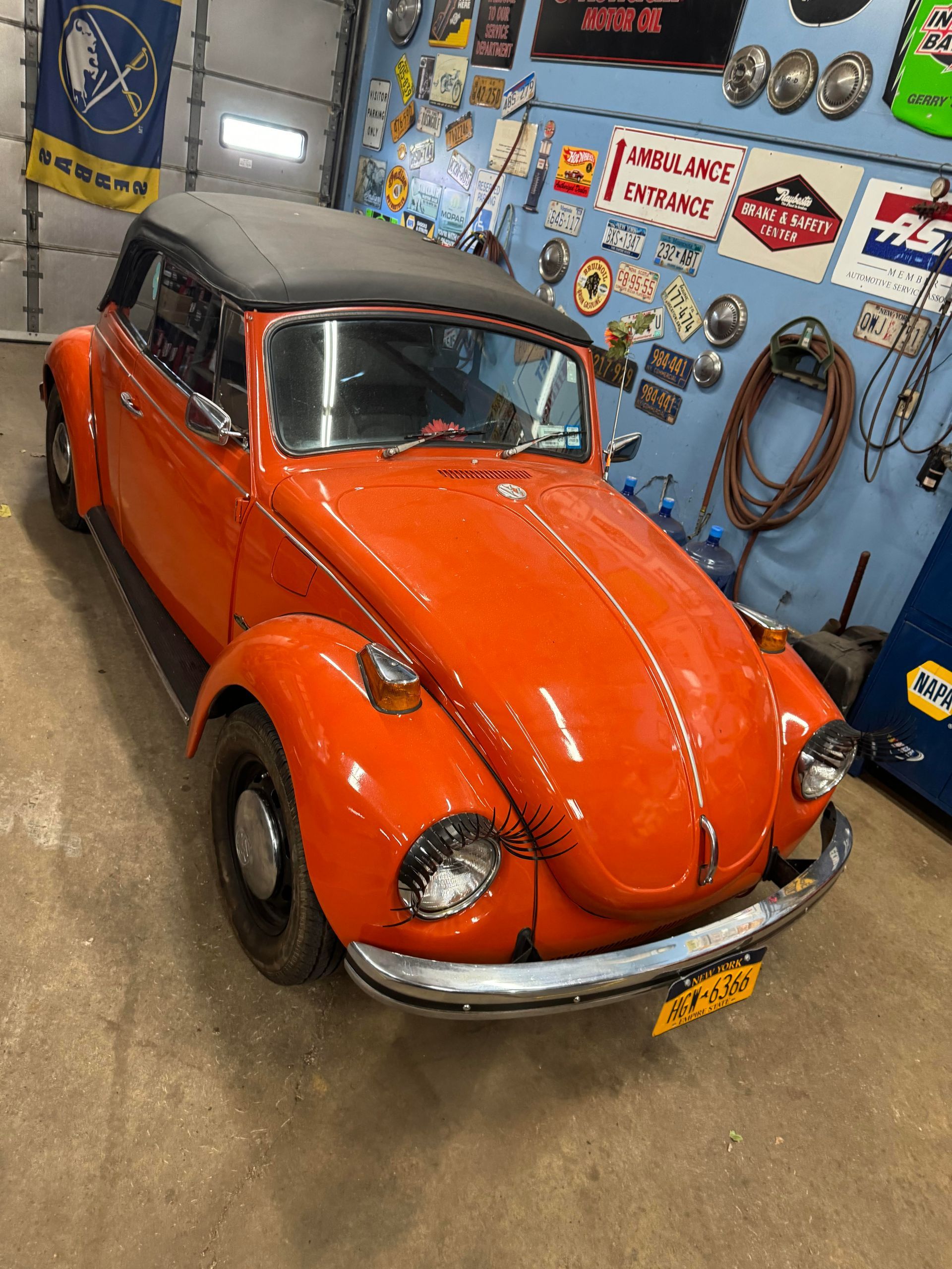 Orange Volkswagen Beetle convertible in a garage, black top.
