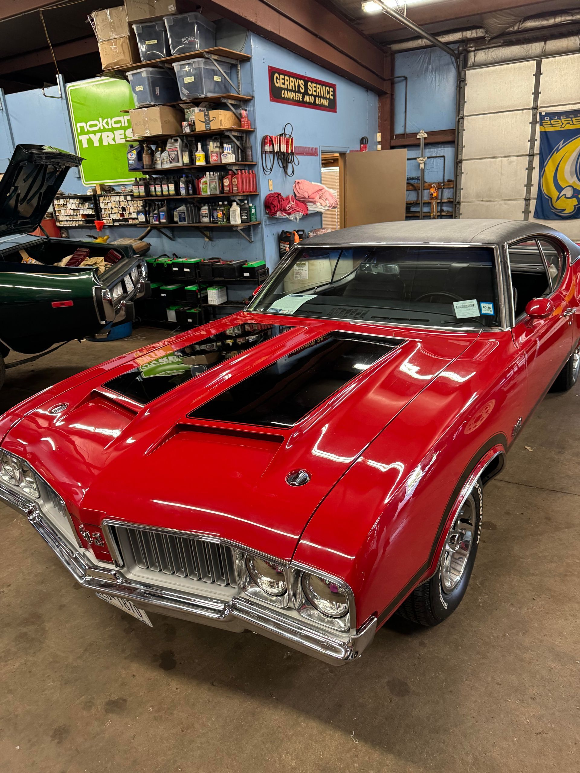 Red classic car with black stripes on hood, in a garage.