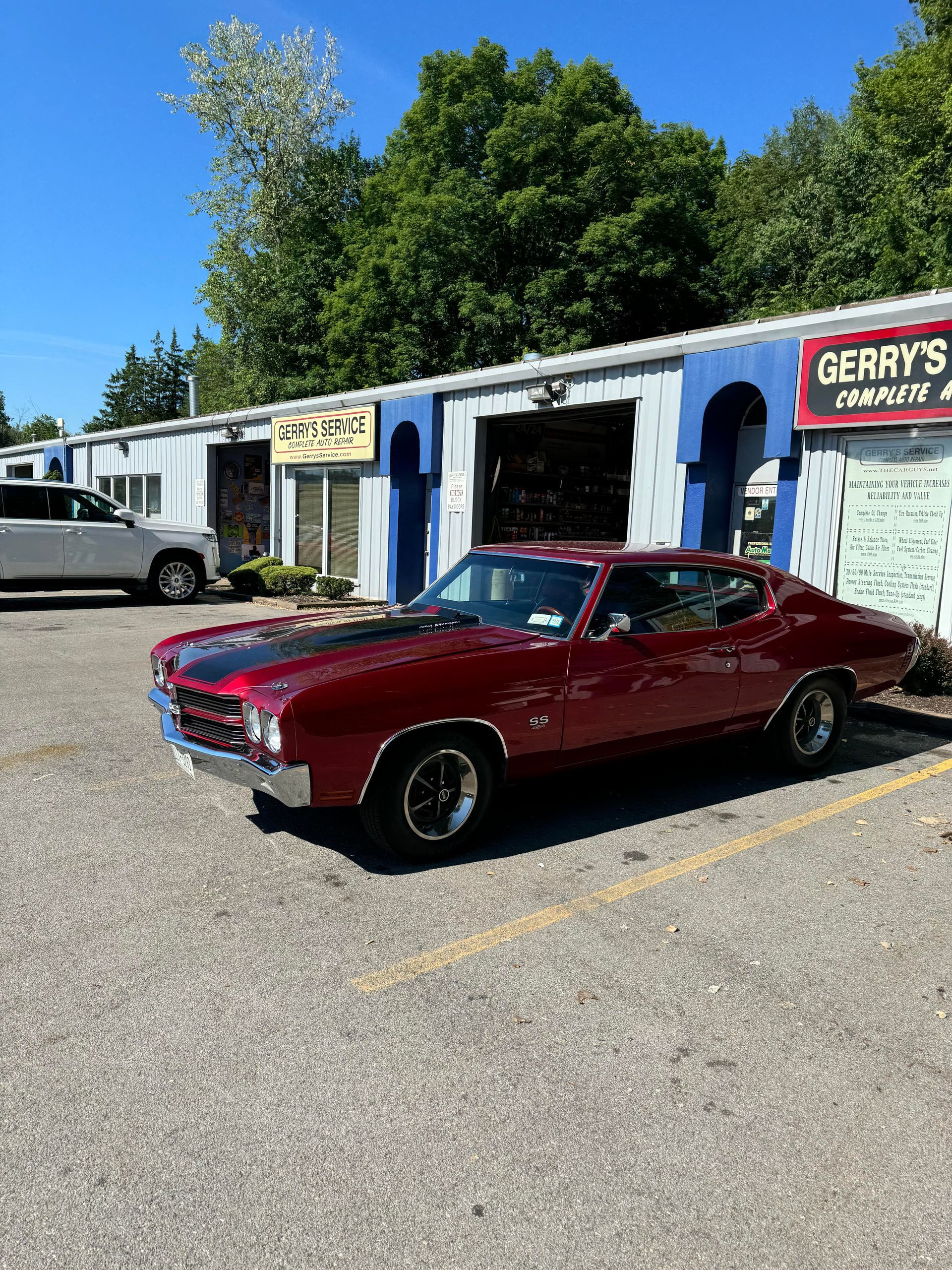 Red classic car parked outside a repair shop, sunny day.