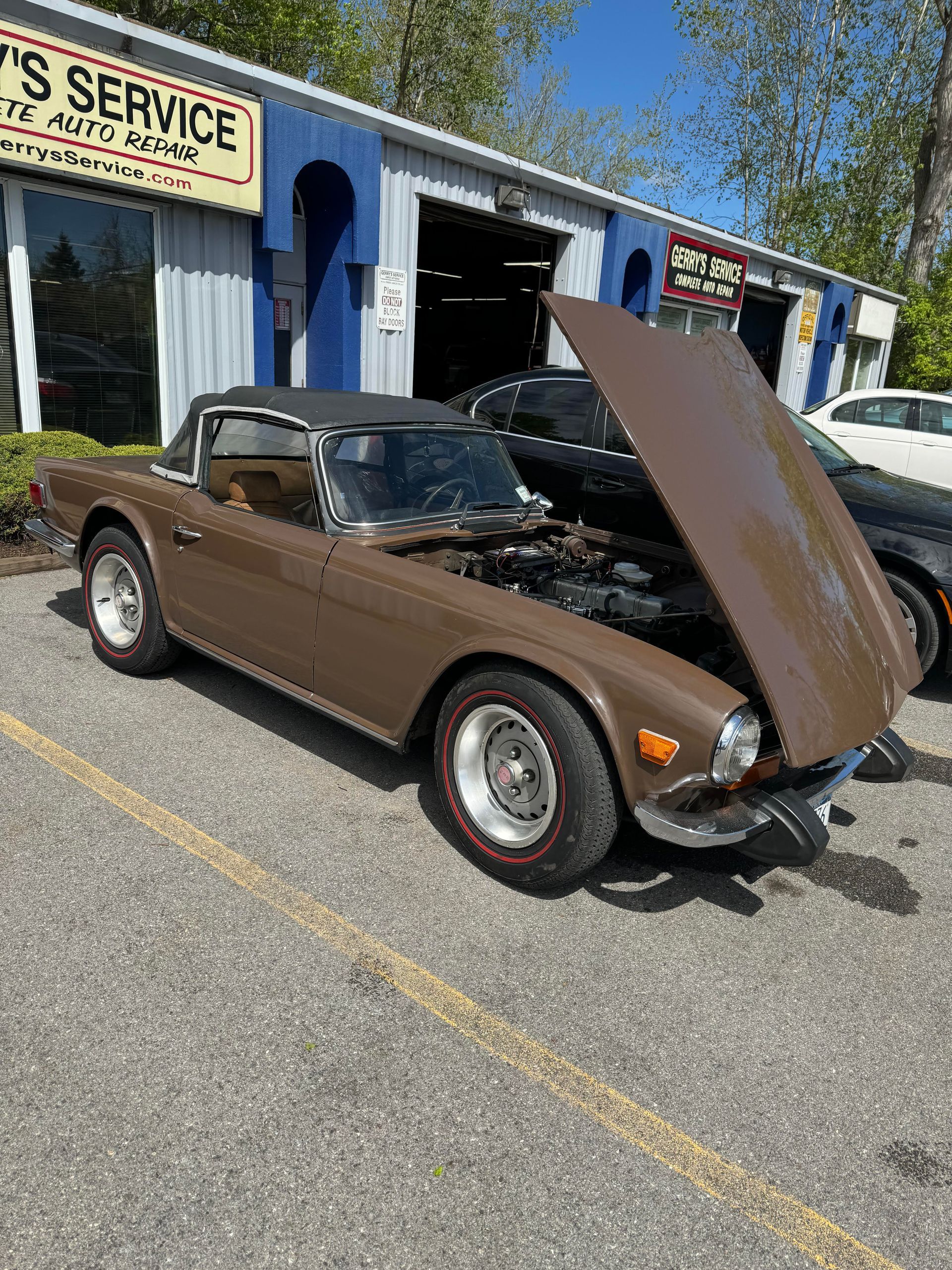 Brown convertible car with hood up, in front of a service garage.