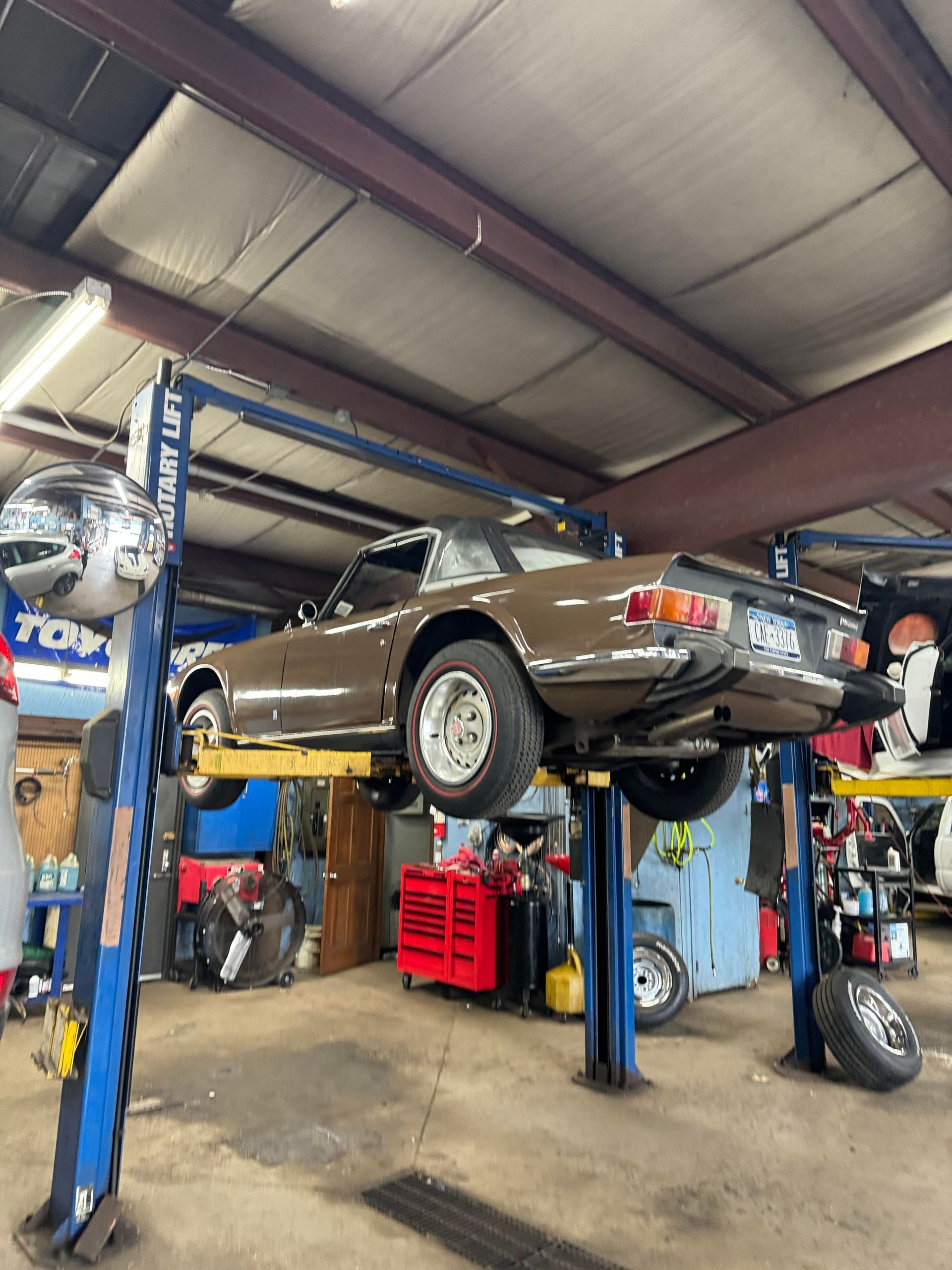 Brown classic car elevated on a blue car lift inside a garage.