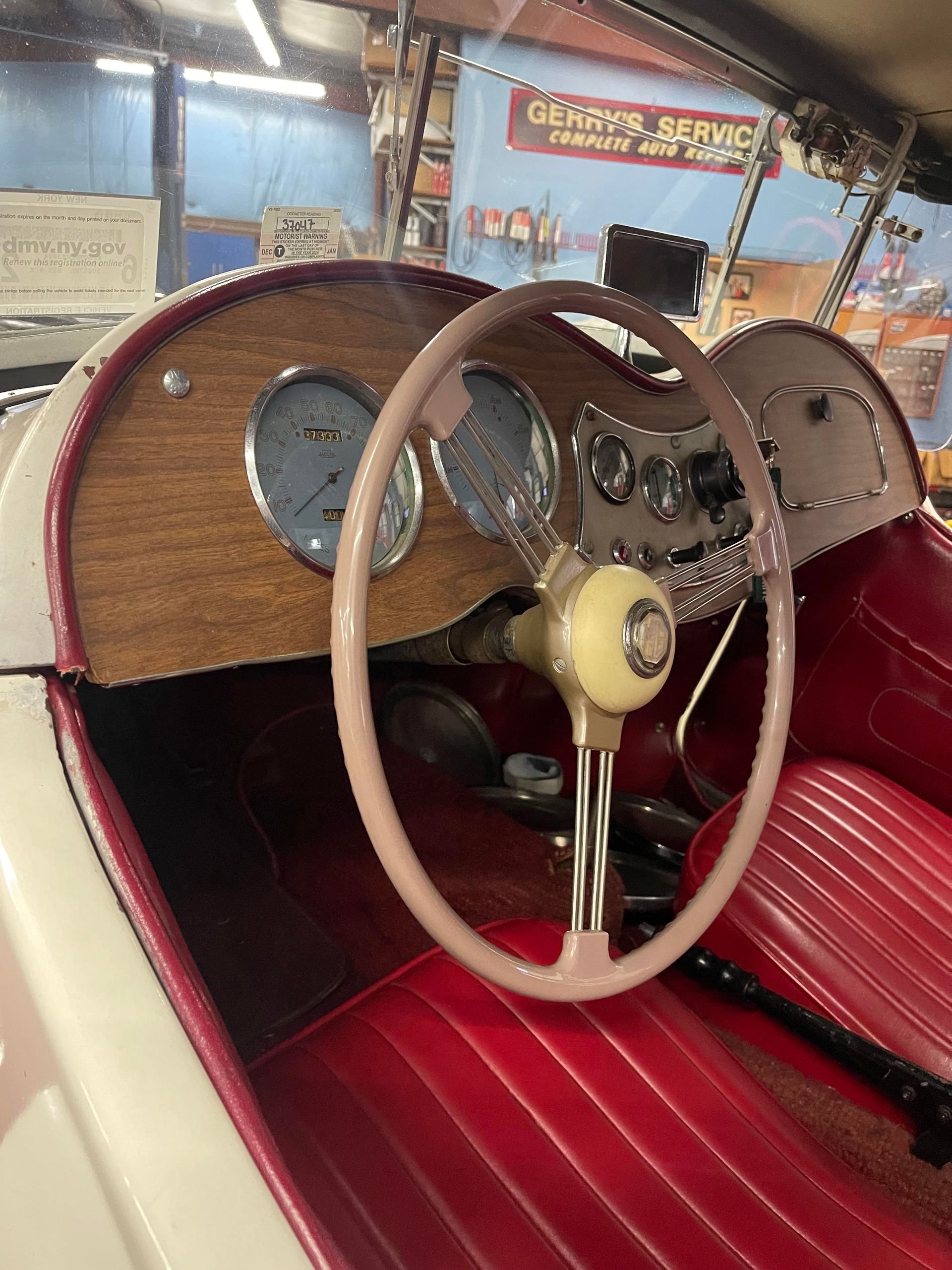 Classic car interior with wood dashboard, pink steering wheel, and red seats.