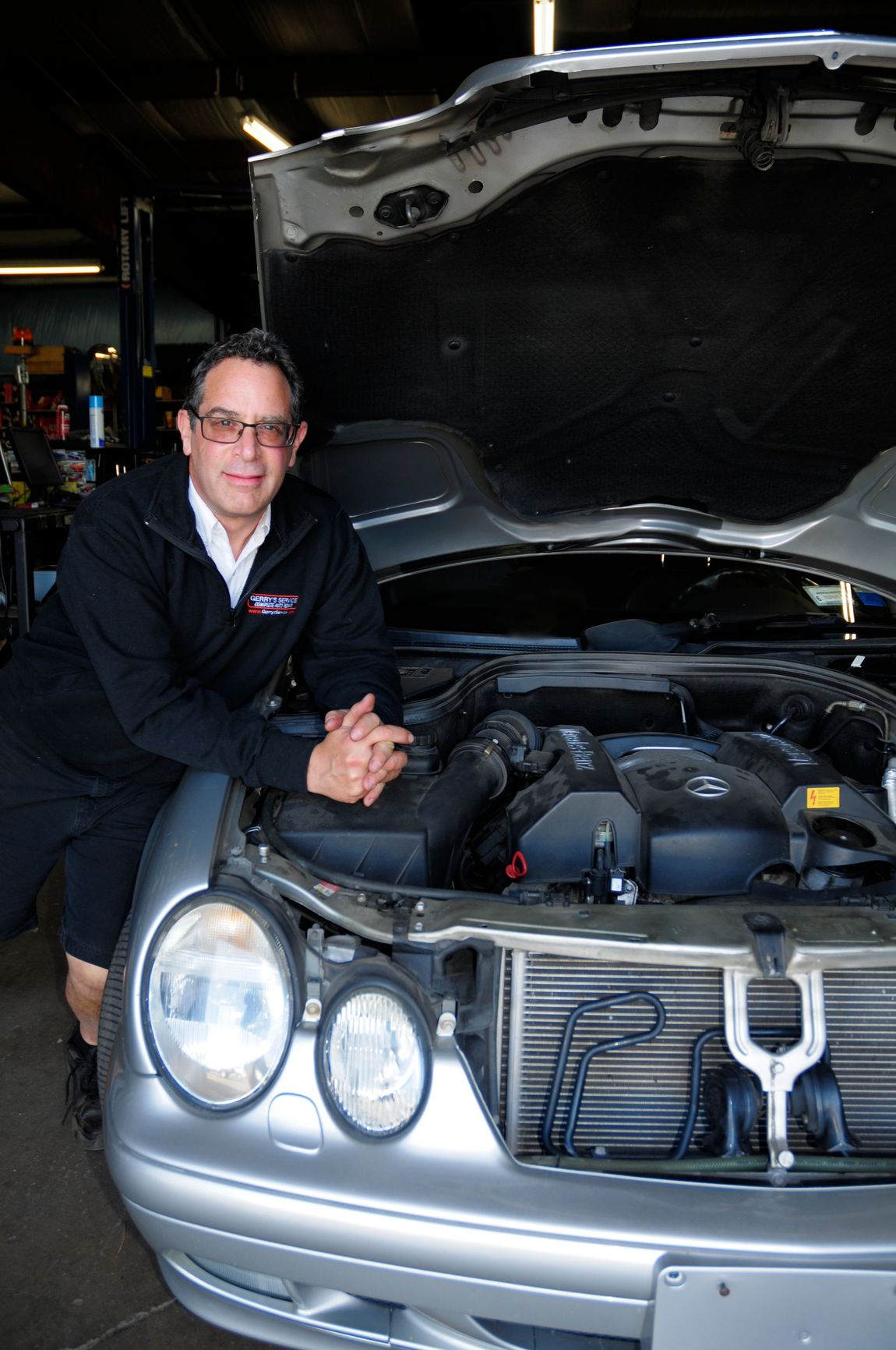 Mechanic leaning on a car with the hood up, in a garage.