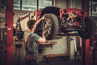 Mechanic working on a red classic car raised on a lift in a garage.