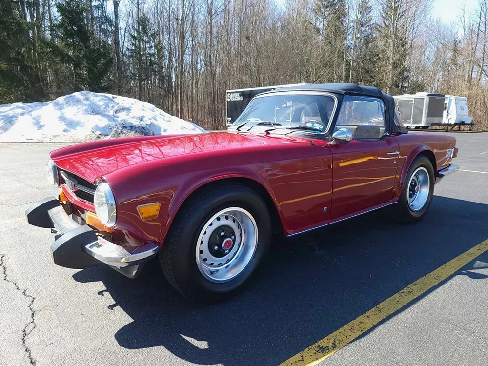 Red convertible car, parked on asphalt, near snow. Bright sunny day.