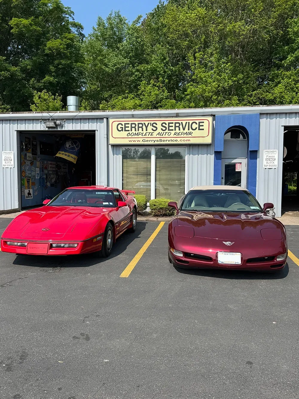 Two red Corvettes parked in front of Gerry's Service automotive shop.