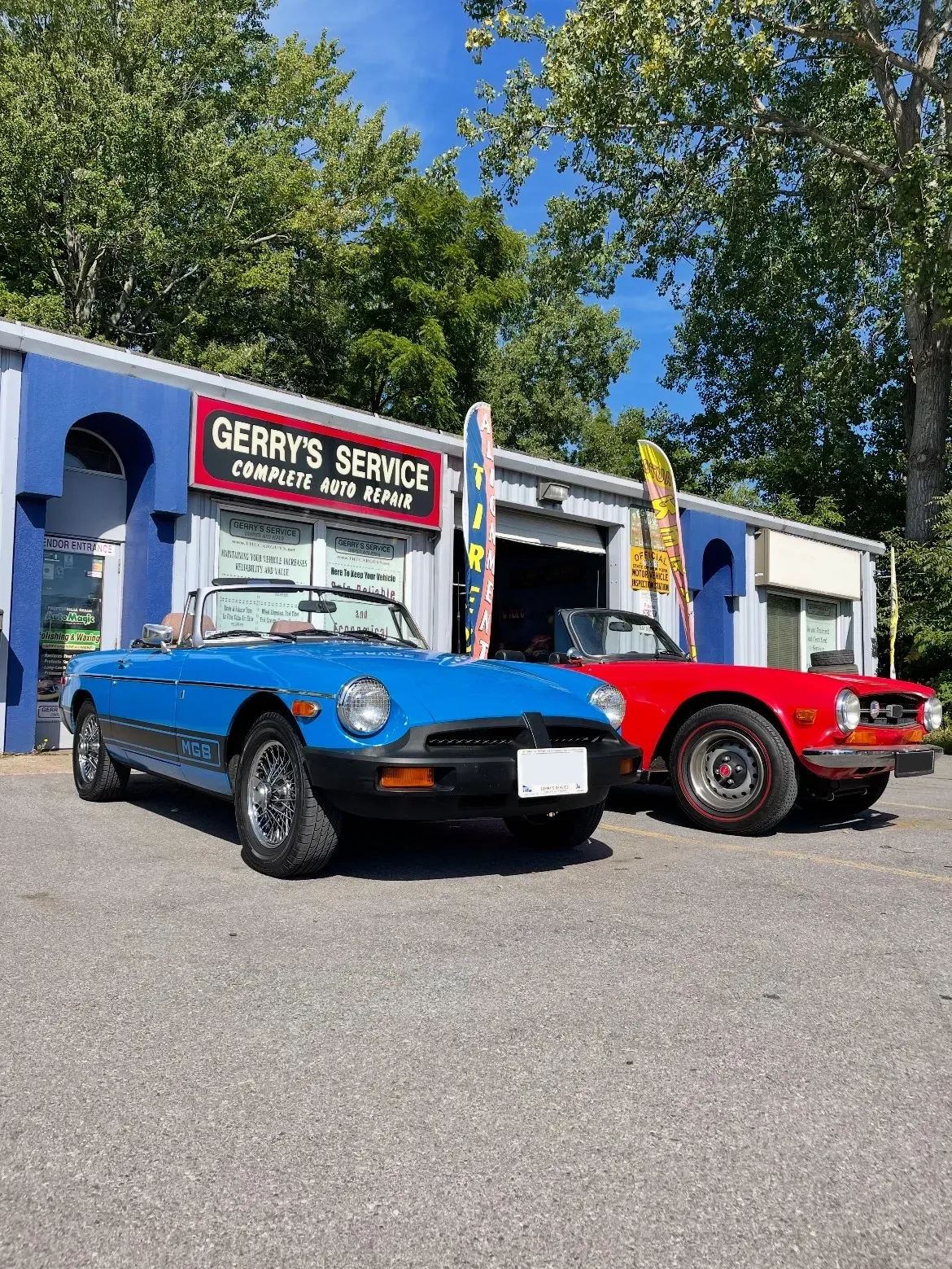 Blue convertible and red car parked in front of Gerry's Service, a car repair shop.