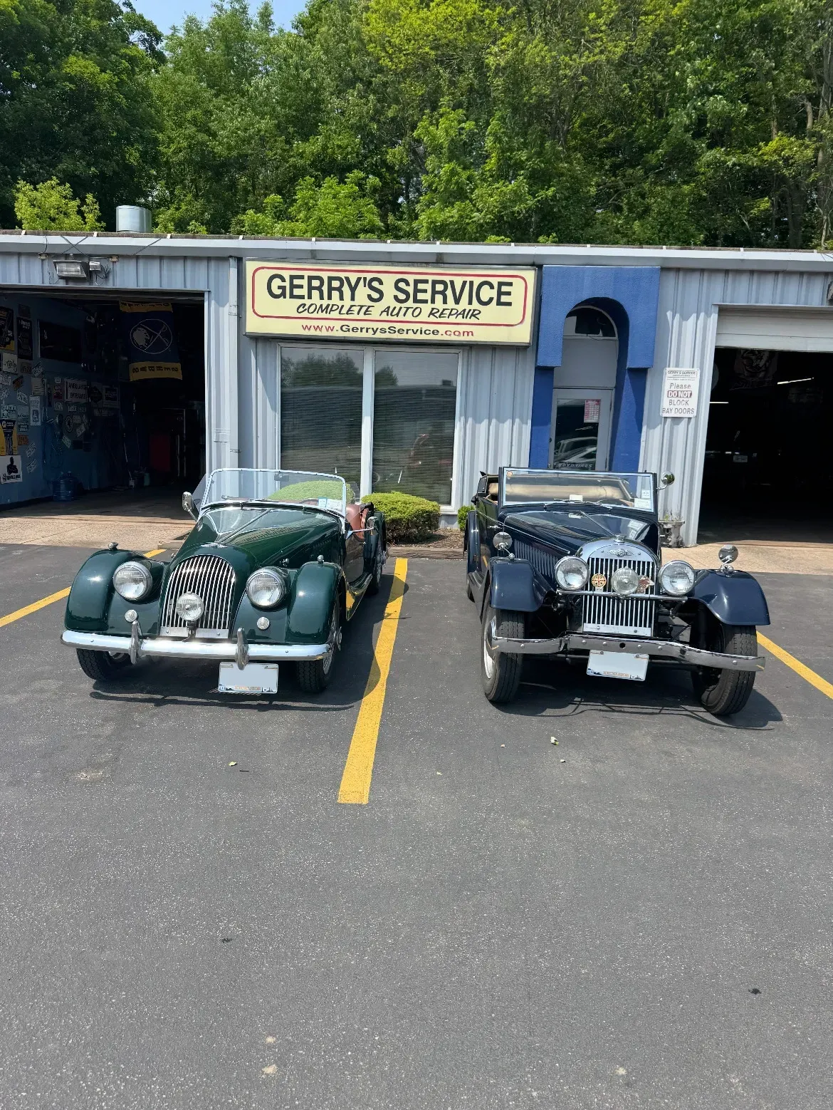 Two classic cars parked outside Gerry's Service garage, one green, one dark blue.