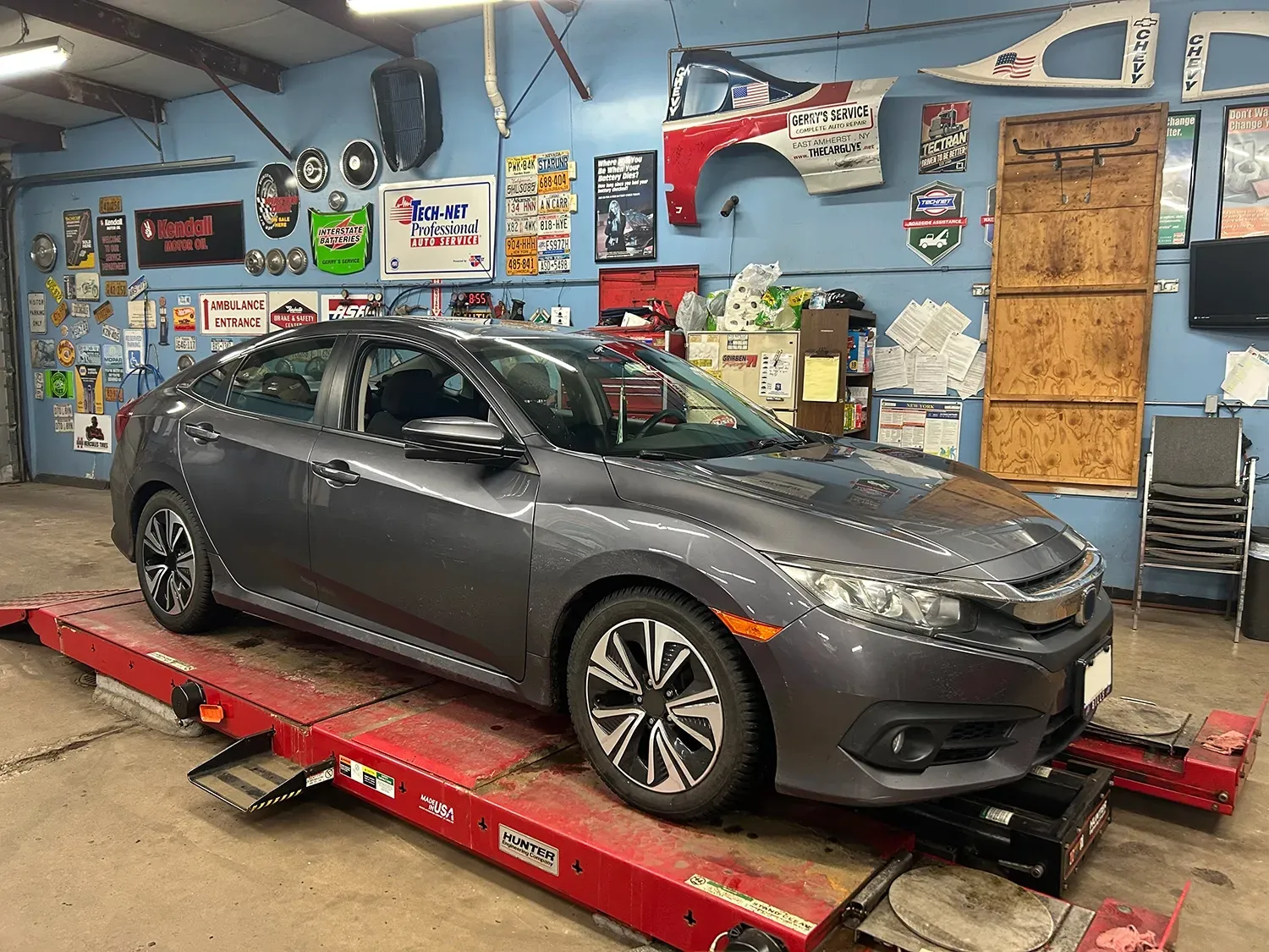 Gray Honda Civic on a red lift inside an auto repair shop.