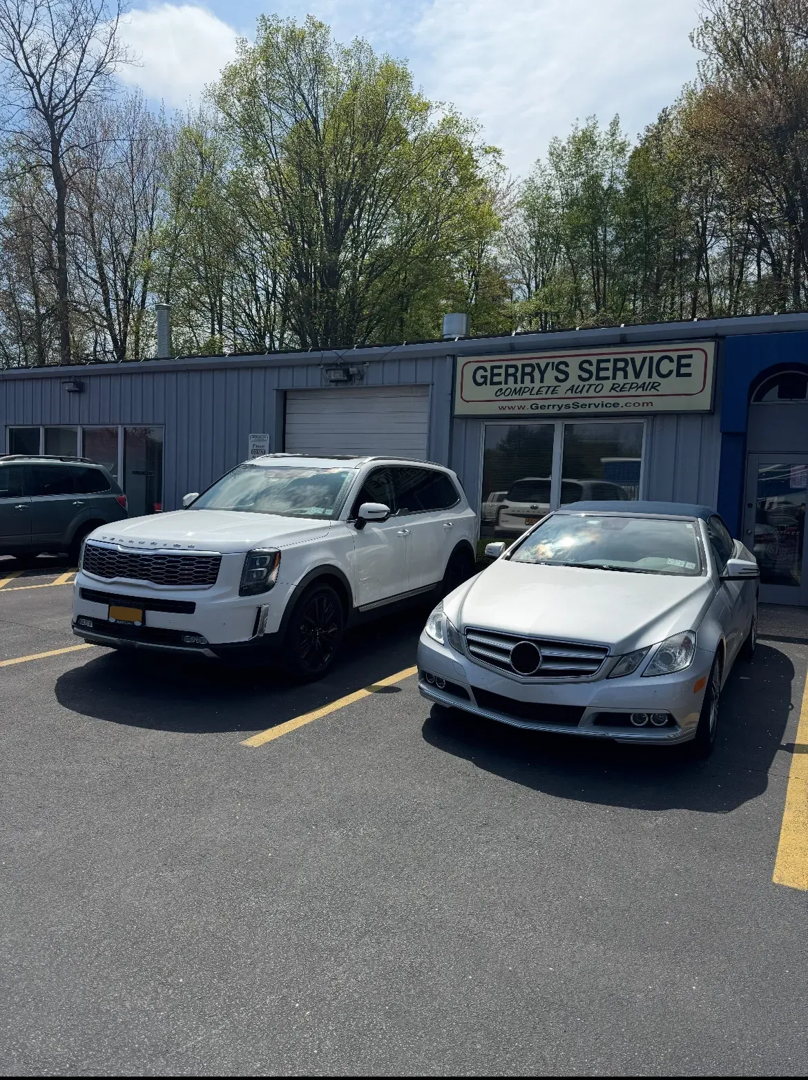 White Kia Telluride and silver Mercedes parked in front of Gerry's Service garage.