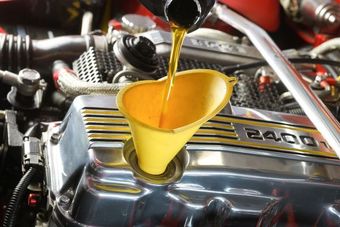 Yellow funnel pouring oil into an engine, likely during an oil change.