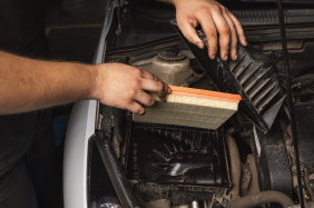Person replacing an air filter in a car engine compartment.