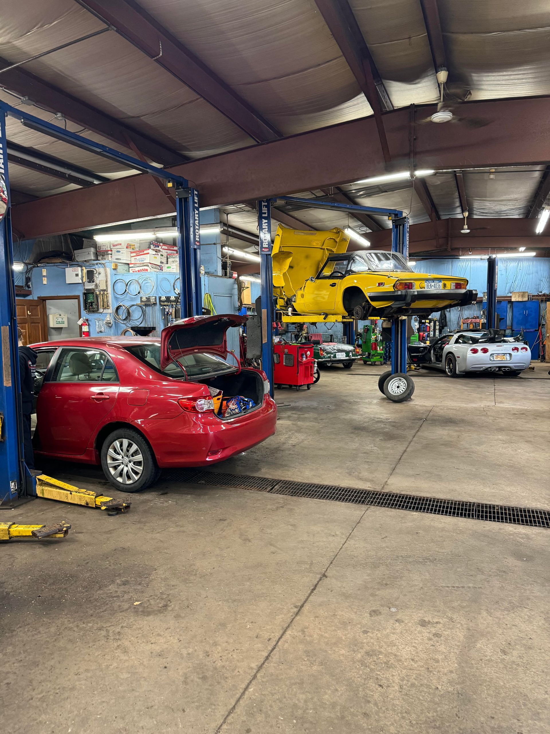 Car repair shop with a red car and a yellow car on lifts, tools on the wall.