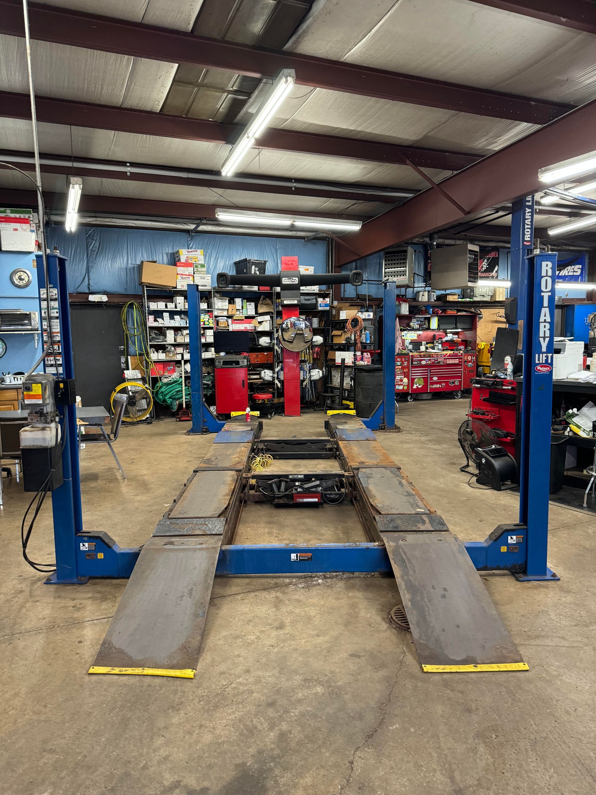 Blue car lift in a cluttered auto repair shop.