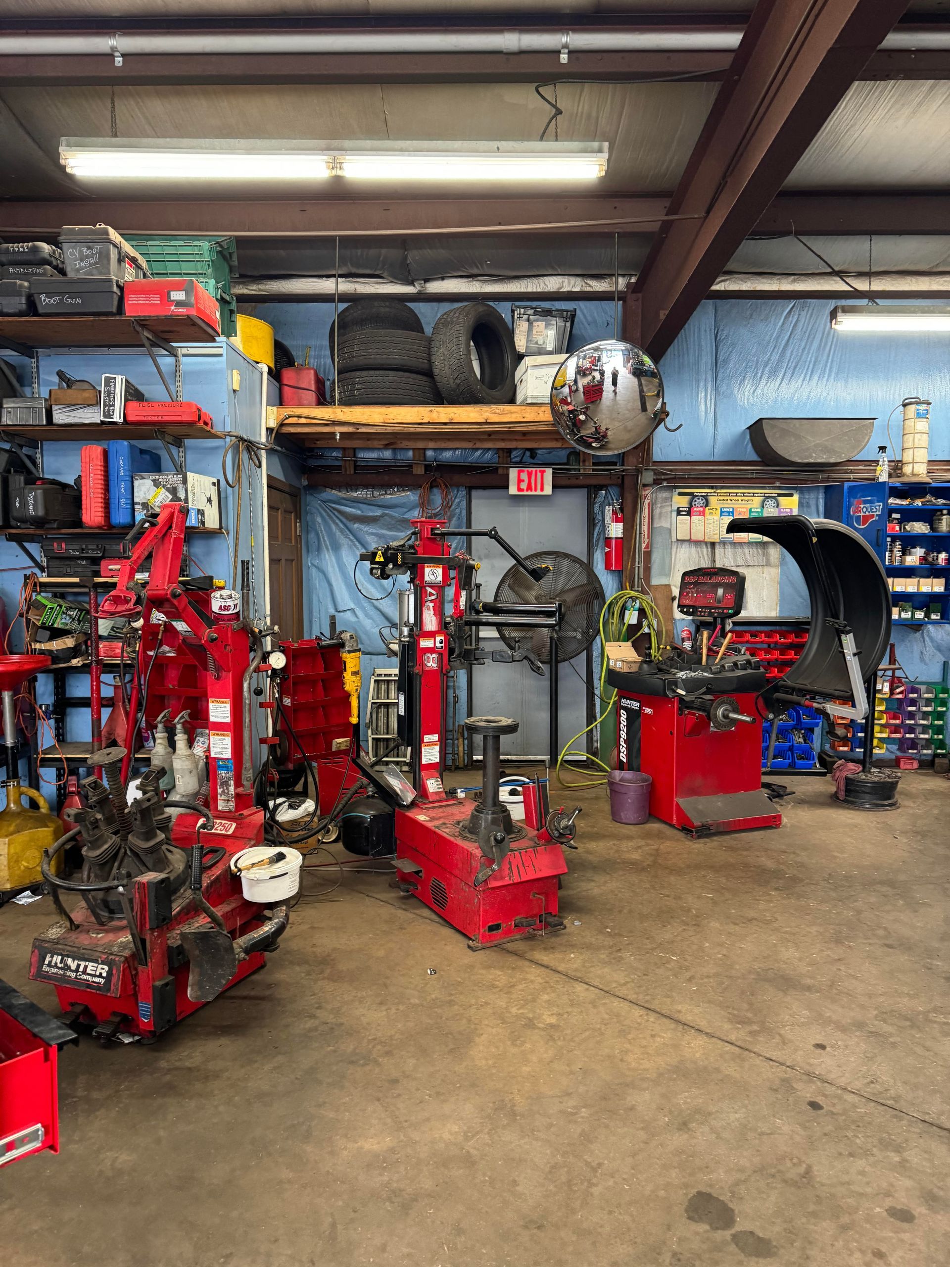 Garage interior with tire equipment and tools; red machines, shelves of items, and tires.
