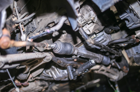 Undercarriage view of a car's steering rack and suspension components, showing tie rods, boots, and control arms.