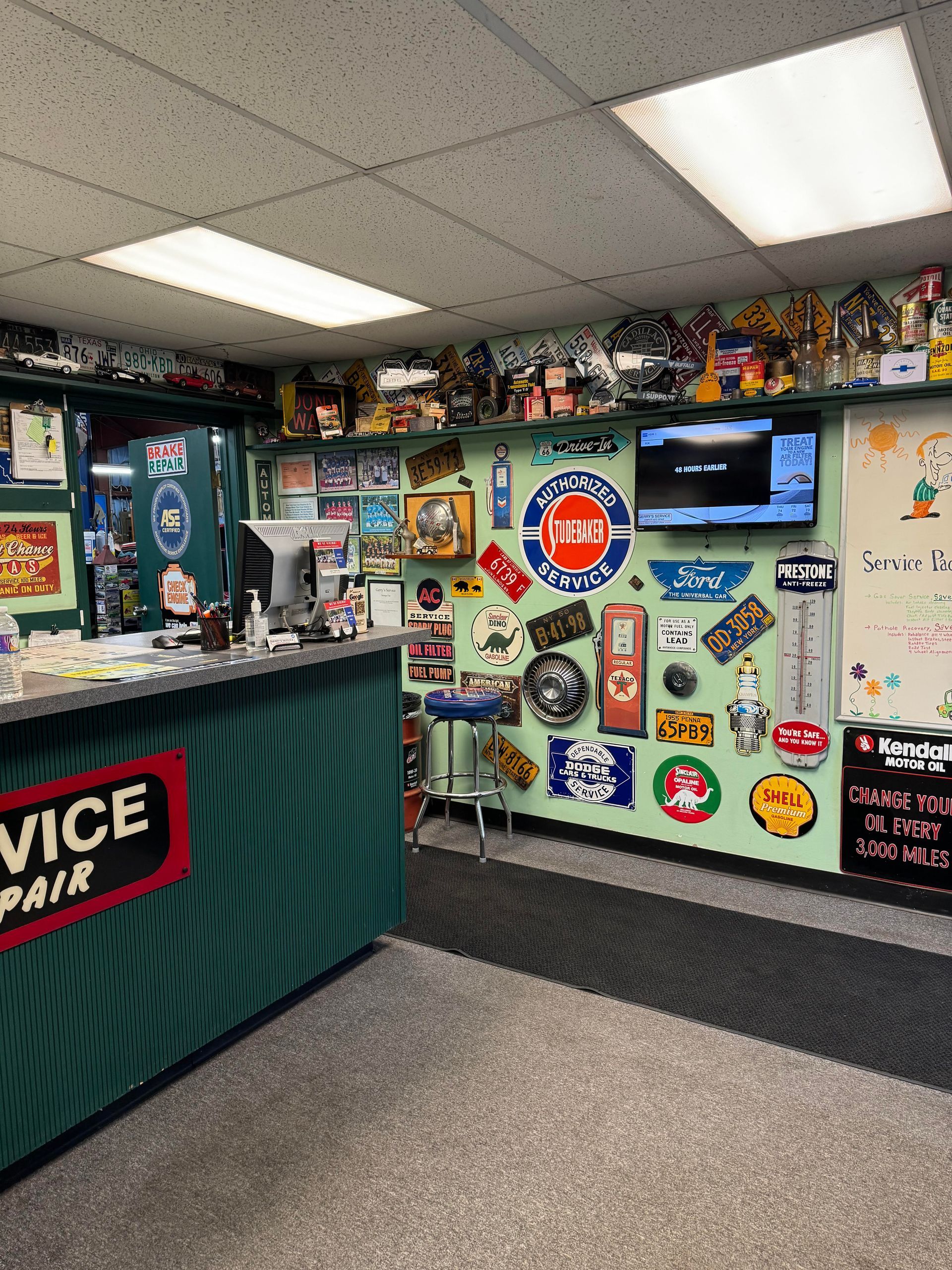 Interior of an auto repair shop with a reception desk, green walls decorated with signs, and a TV.