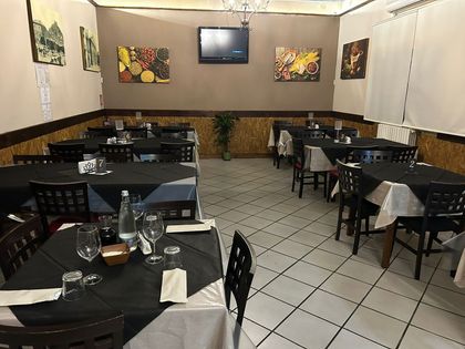 Sala da pranzo vuota di un ristorante con tovaglie nere, pavimento piastrellato e opere d'arte alle pareti.